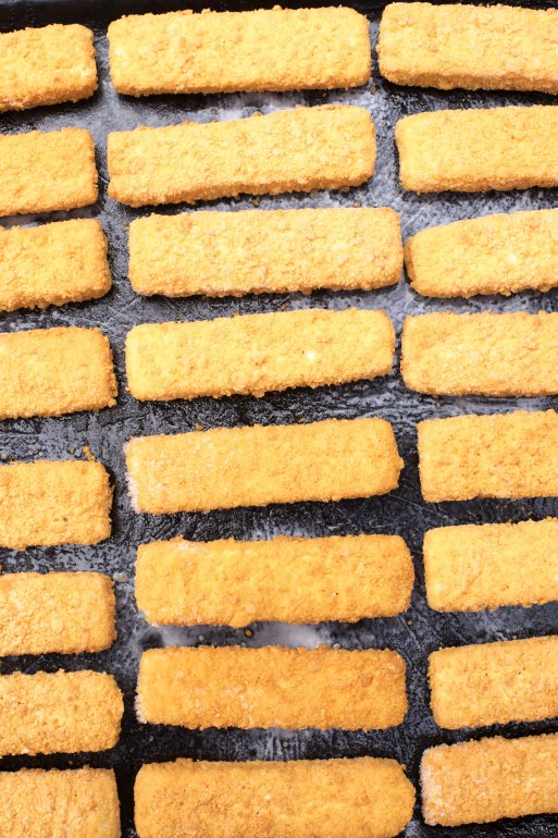 Frozen fish fingers laid out in neat rows to defrost for oven baking, viewed from above in a catering concept