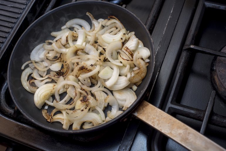 Fresh sliced white onions frying in a pan over a gas hob in the kitchen while preparing dinner
