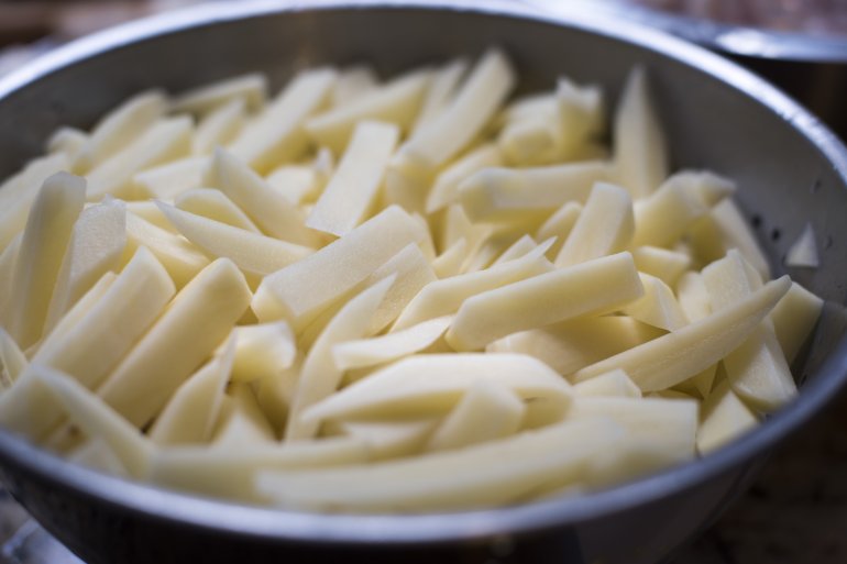 Sliced fresh potatoes in a metal bowl ready to make French fries or fried chips, close up view