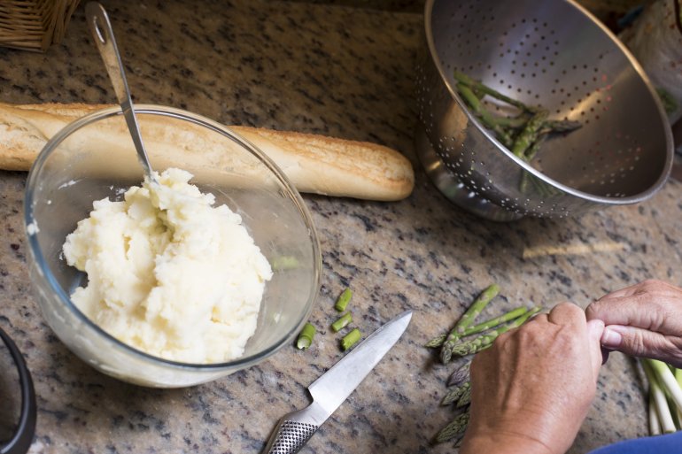 Man preparing the evening meal with mashed potato and green asparagus tips standing ready as he chops the leeks over a marble kitchen counter
