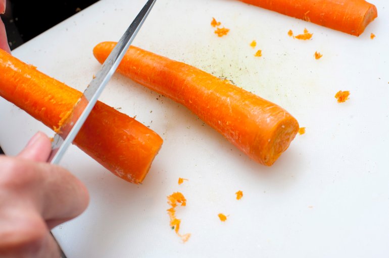 Man scraping carrots with a knife preparing them for cooking as a vegetable or as a salad ingredient