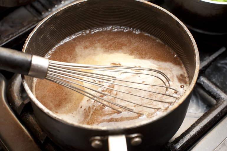 Close up view of brown gravy simmering in sauce pan atop gas range as wire whisk rests inside it