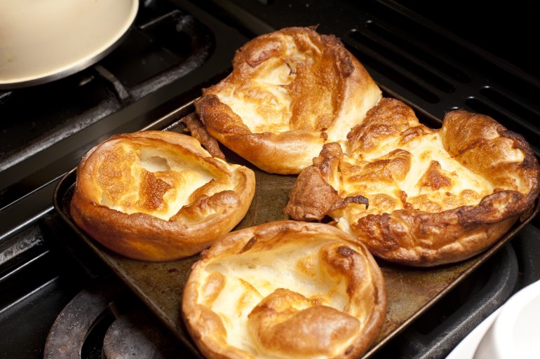 Close up on four freshly baked round Yorkshire pudding buds on square tray on top of slove