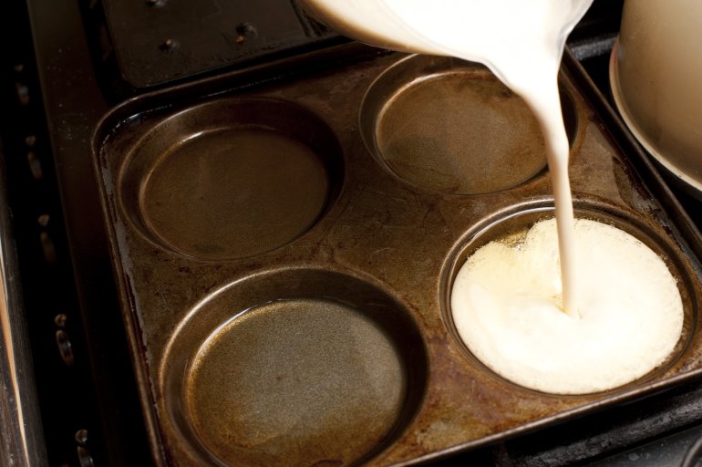 Pouring Yorkshire pudding batter into a pan or baking tray with individual moulds, close up view