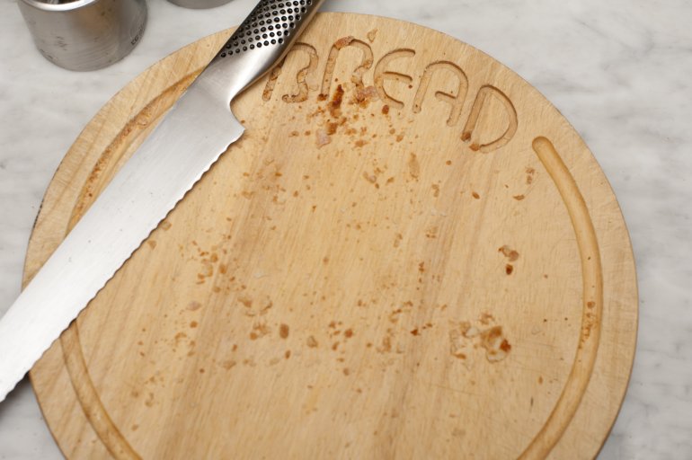 Crumbs and a stainless steel knife on a circular bread board viewed from above after cutting fresh bread
