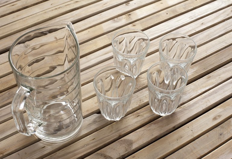 Clean empty transparent glass jug and four tumblers on a rustic slatted wooden table