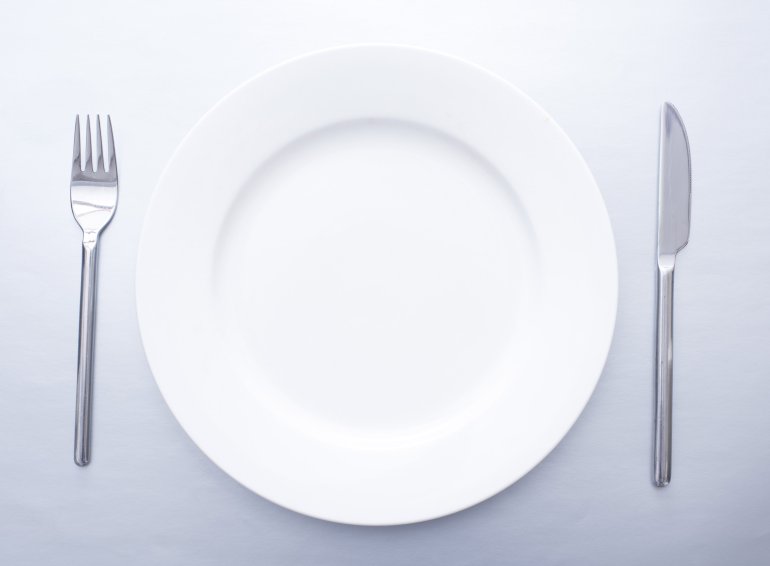 Plain simple place setting with empty white plate flanked by a silver knife and for viewed from overhead