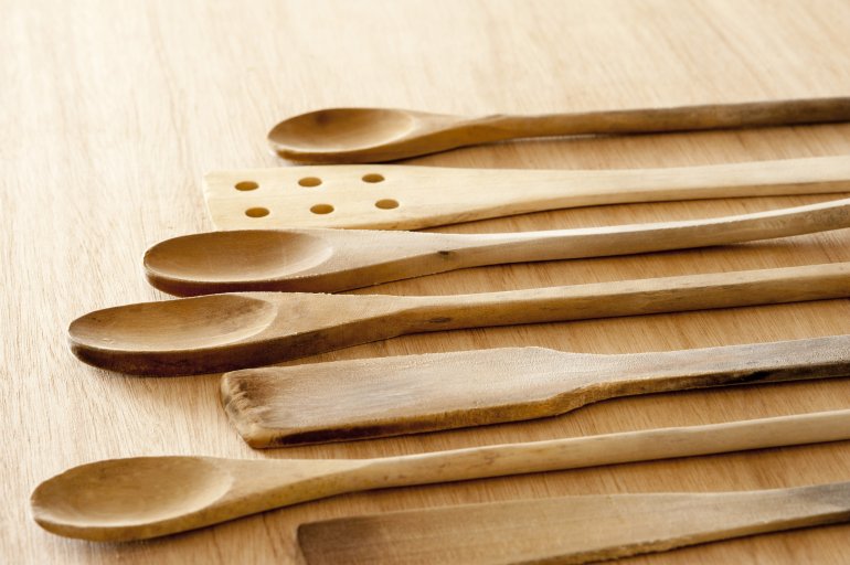 Selection of plain wooden rustic kitchen utensils with assorted spoons, spatulas and strainer in a receding low angle view on a wooden table