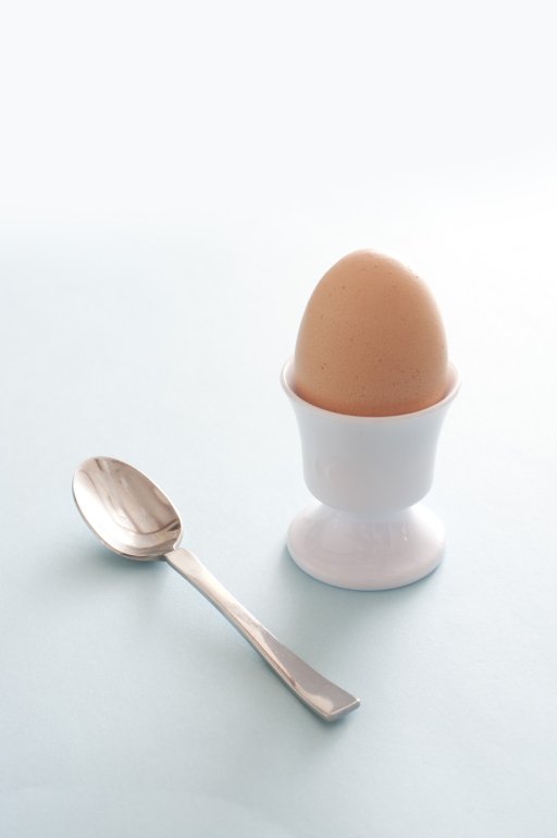 Fresh brown boiled egg for breakfast served in a white ceramic egg cup with a silver spoon