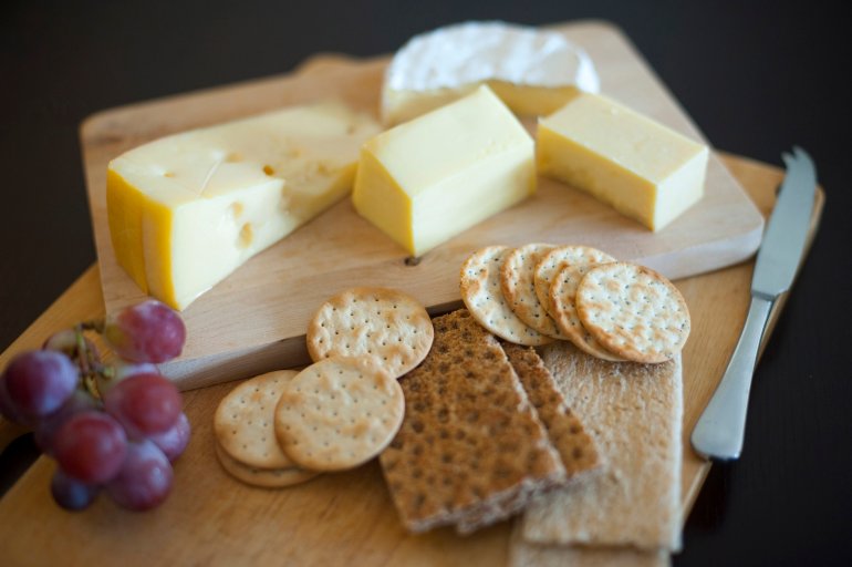 Cheese and biscuit platter with portions of assorted cheeses, crackers and water biscuits and a small bunch of fresh grapes on a dark background