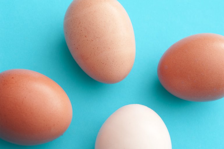 Four fresh raw whole eggs pointing towards the center on a blue background in different shades of brown through white