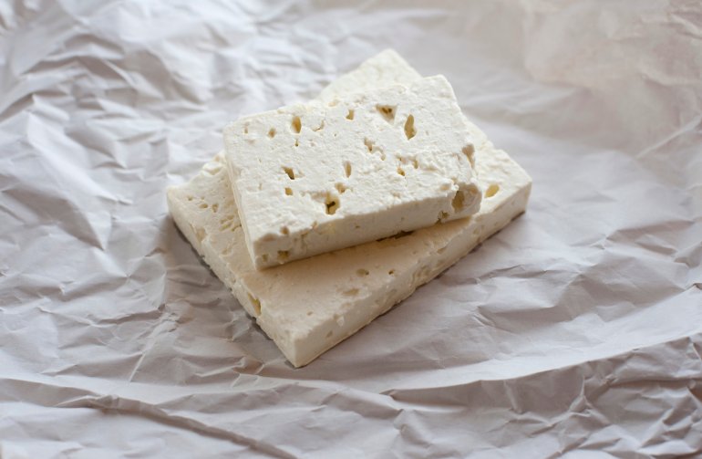 Two portions of feta cheese, a traditional Greek cheese made for goat or sheep milk, lying on a crumpled sheet of white paper