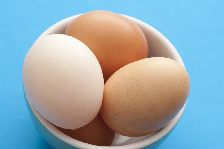 Farm fresh eggs in a little white ceramic bowl ready to be used for a healthy breakfast or baking , high angle over blue