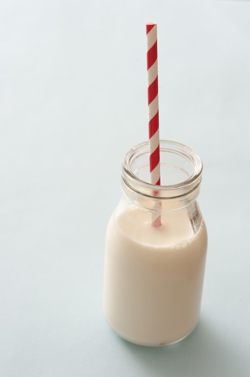 Little jar of milk with red and white straw stuck on top over neutral background with copy space