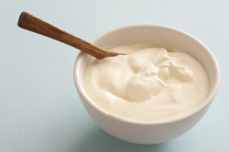 Plain white ceramic bowl of sour cream with a spoon over a grey background for use as a topping and ingredient in cooking
