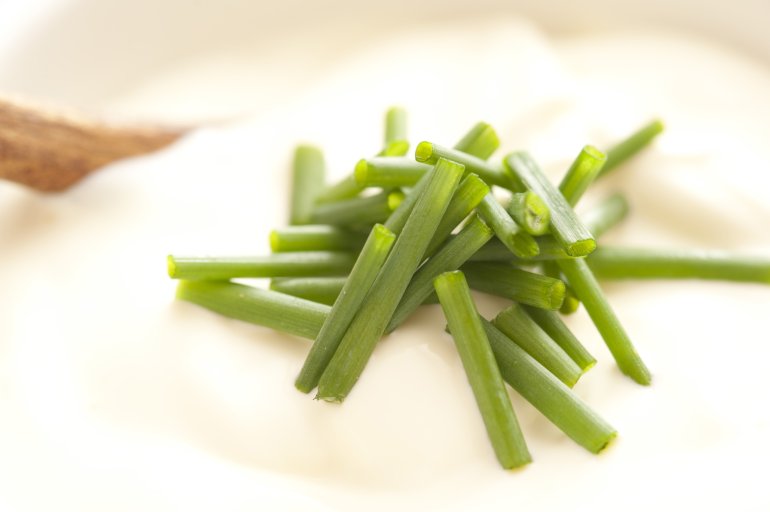 Chopped fresh green chives used as a garnish on a bowl of sour cream in a close up view on the herbs