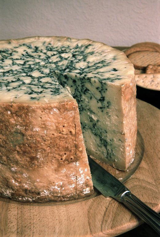 Stilton cheese, an English blue veined cheese made with added cream which has a distinctive flavour and high fat content, closeup view of a wheel with a wedge removed