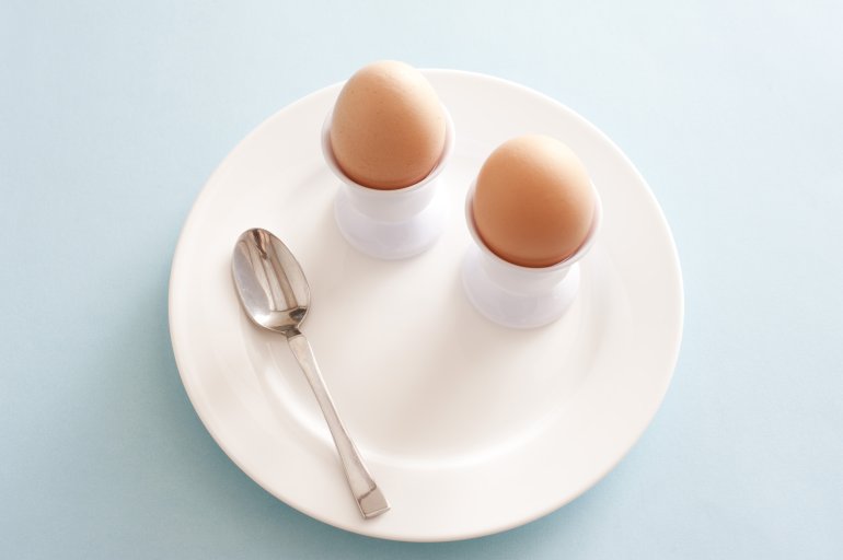 Two boiled fresh brown farm eggs for a healthy breakfast served on a white plate in eggcups in a high angle view