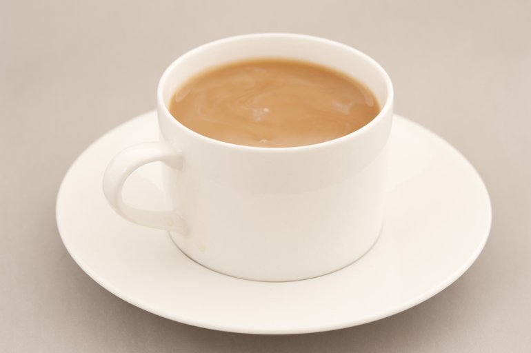Cup of freshly brewed milky coffee in a generic white cup and saucer over a beige background