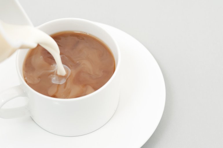 Pouring milk from a generic white milk jug into a cup of strong filter coffee, high angle close up view with copyspace