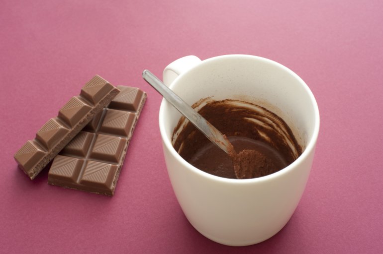 Cup of delicious rich melted hot chocolate for winter standing on a red background with bars of chocolate candy used in the recipe, high angle view