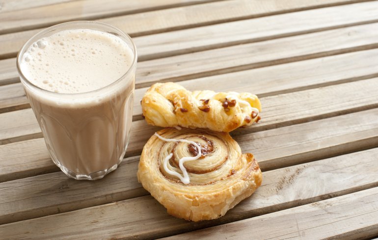 Latte coffee with fresh apple and cinnamon Danish pastries standing outdoors on a wooden garden table for an early morning snack