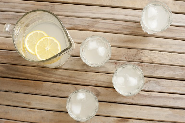 Delicious homemade fresh lemonade rich in vitamin C served cold with ice in a jug and tumblers viewed from overhead on a wooden garden table