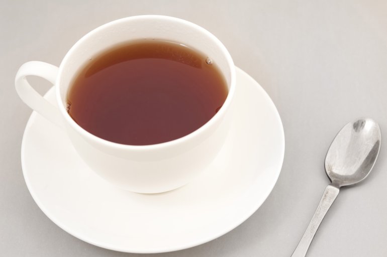 Cup of freshly brewed black tea in a generic white ceramic cup and saucer with a teaspoon alongside, high angle view