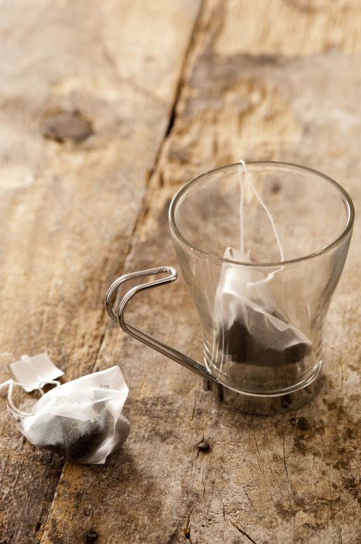 Glass mug with teabags for making a fresh brew standing on a rustic wooden table, high angle view