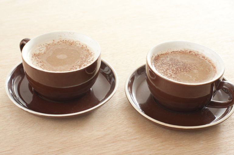 Two brown ceramic cups and saucers of fresh cappuccino coffee with a rich milky foam served on a wooden table with gradient color to white