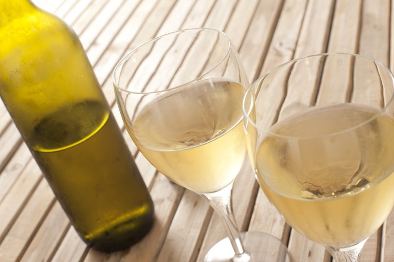 Two glasses of chilled white wine with an unlabelled half full wine bottle alongside, close up view on a slatted wooden table with copyspace