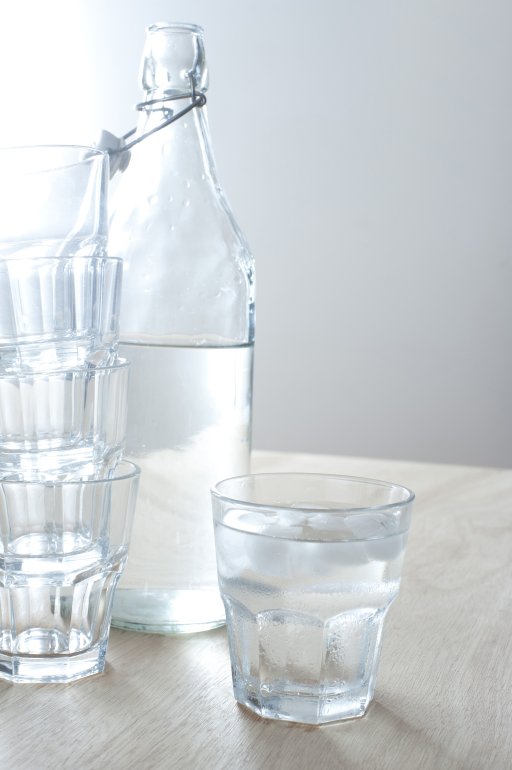 Refreshing cold pure water served in a glass bottle with one full tumbler and a stack of empty glasses alongside, healthy drink with copyspace