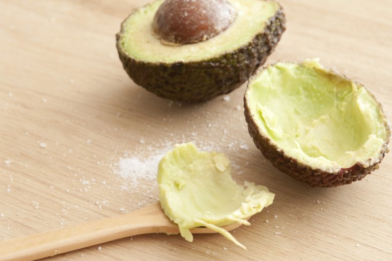 Close-up of cut fresh avocado and spoon on wooden table