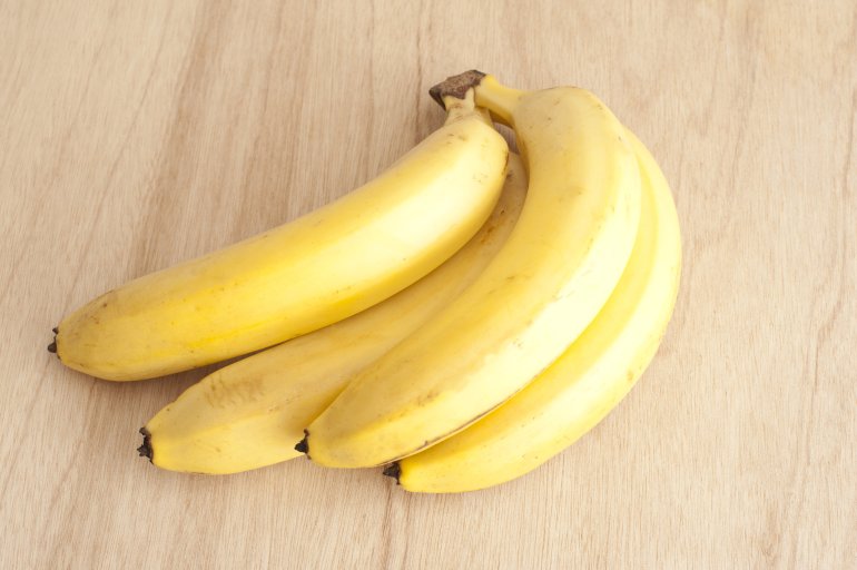 High Angle Close Up Still Life of Bunch of Four Ripe Yellow Bananas on Wooden Background