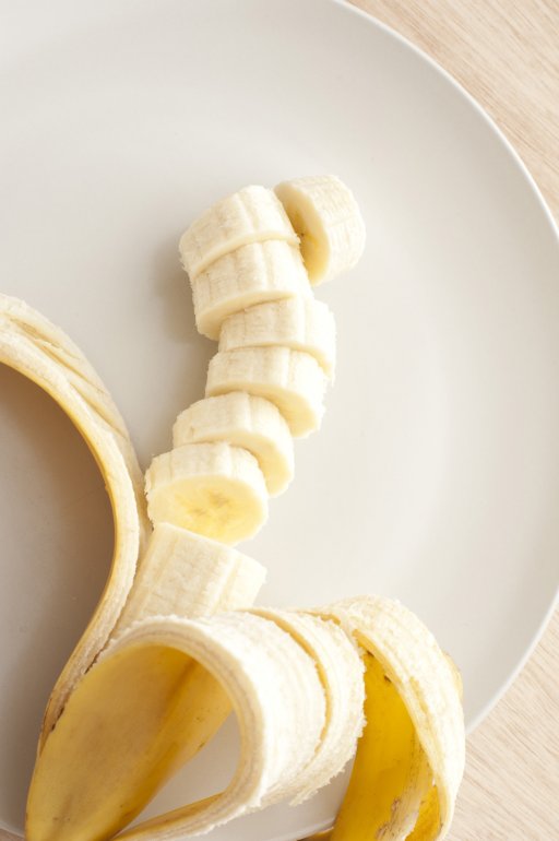 High Angle Close Up Still Life of Ripe Banana Partially Peeled and Sliced on White Dinner Plate with Copy Space