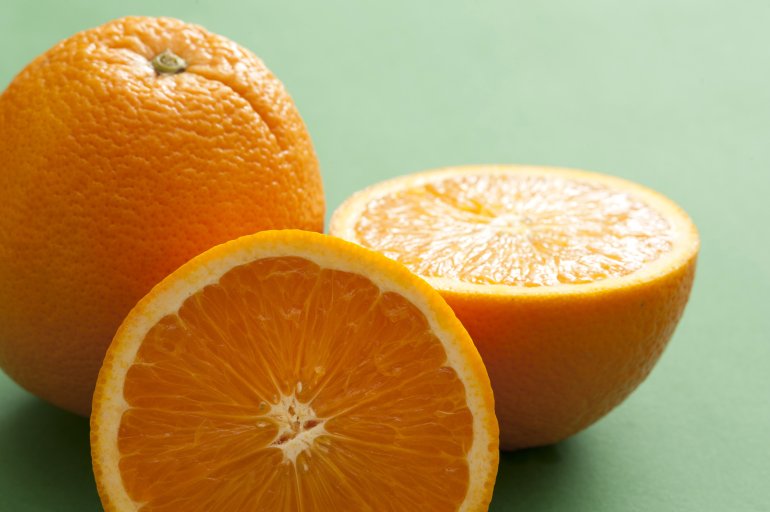 Close-up of one whole and cut orange on green background