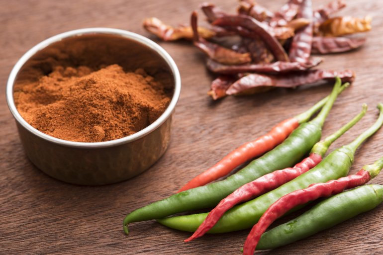 Red hot chilli powder with fresh and dried pods on a wooden table for use as a pungent hot spice in cooking