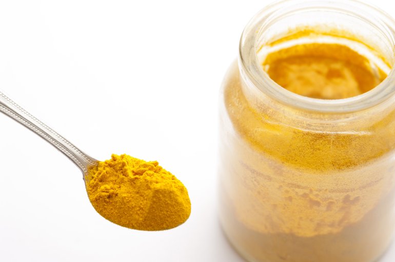A spoon and a jar of ground turmeric in close-up on white background