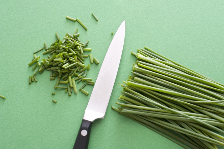 Sharp kitchen knife with chopped fresh chives over a green background ready to use as a culinary garnish