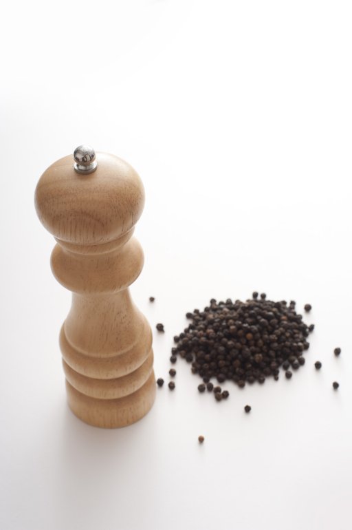 Heap of dried black peppercorns alongside a wooden mill or grinder over a white background with copy space