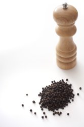 Black peppercorns alongside a grinder
