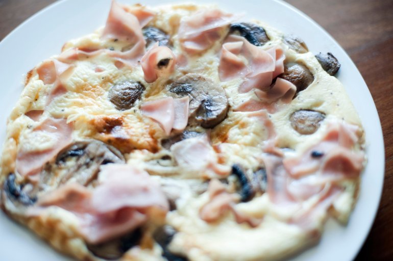 Delicious lightly fried serving of ham and mushroom omelette on a plain white plate for a healthy light snack or meal