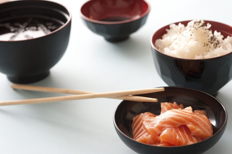 Raw salmon sashimi pieces served with rice and a soy dipping sauce in traditional individual bowls for gourmet Asian cuisine