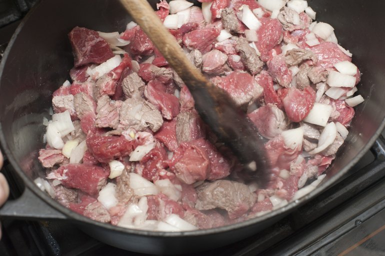 Close up view of a cook browning diced beef and onions in a frying pan using a wooden spoon in preparation for making a stew