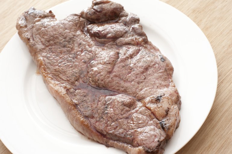 Portion of cooked rump steak served on a white plate, high angle view of the uncut meat