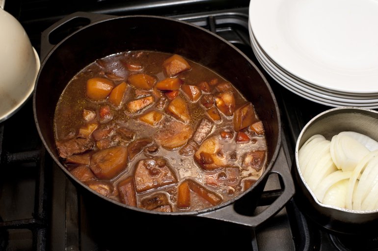Delicious hot soup with potatoes, meat, different vegetables in saucepan on stove. From above