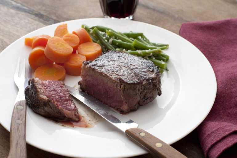 Delicious medallion of thick juicy fillet steak sliced through and served with carrots and green runner beans on a white plate