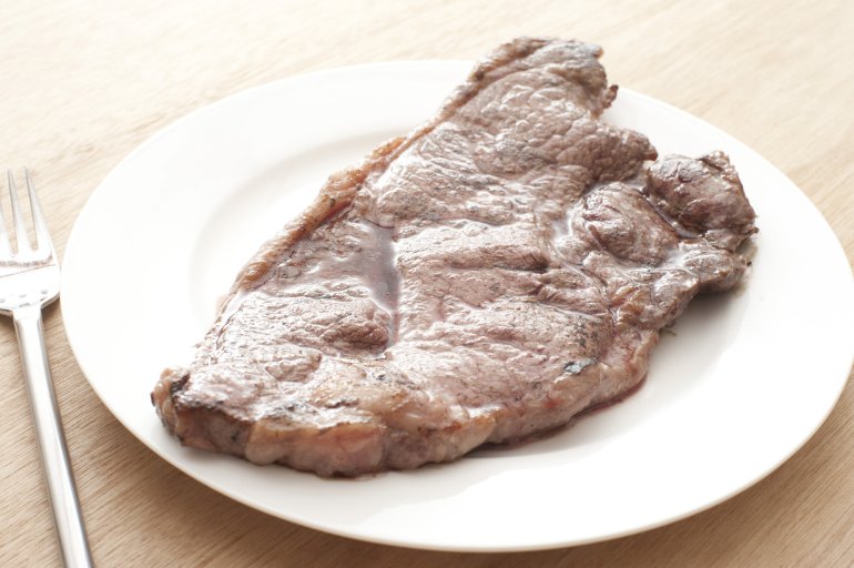 Close-up of tasty roasted beefsteak on white plate with fork