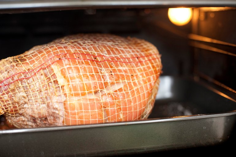 Interior view of a cut of pork roasting in the oven bound in net on a grilling pan