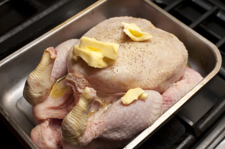 Close-up of whole uncooked chicken with butter and pepper on top in oven